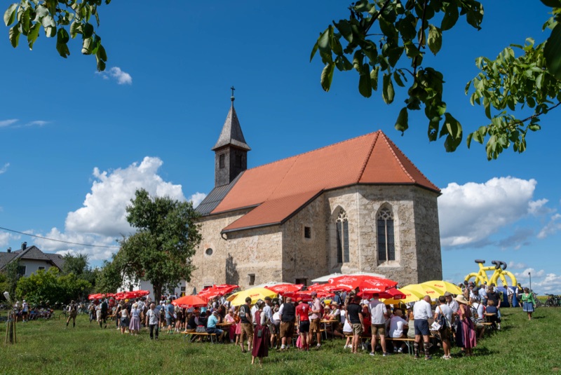 Kösslwanger Kirche mit bunten Sonnenschirmen und Gästen